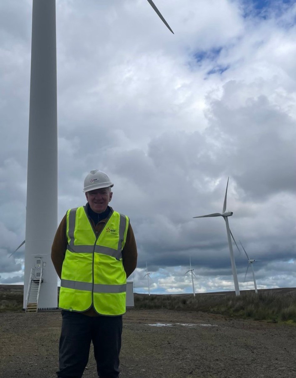 A photo of Ray standing
 by a wind farm